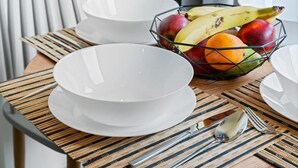 Ein Esstisch mit weißen Tellern, einer Obstschale und einer gewebten Tischmatte.