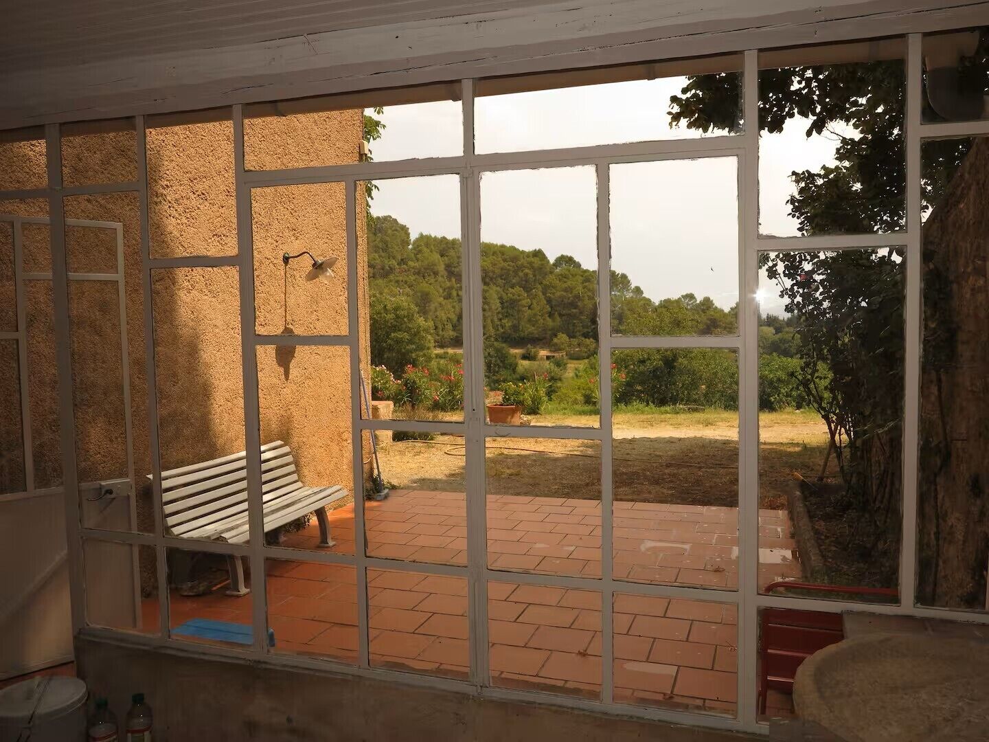 A room with a large window, a bench, and a view of a garden.