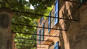 A narrow alleyway with a building featuring a stone facade and green shutters, leading to a grassy area. - Bastide Saint-Martin (Cotignac)