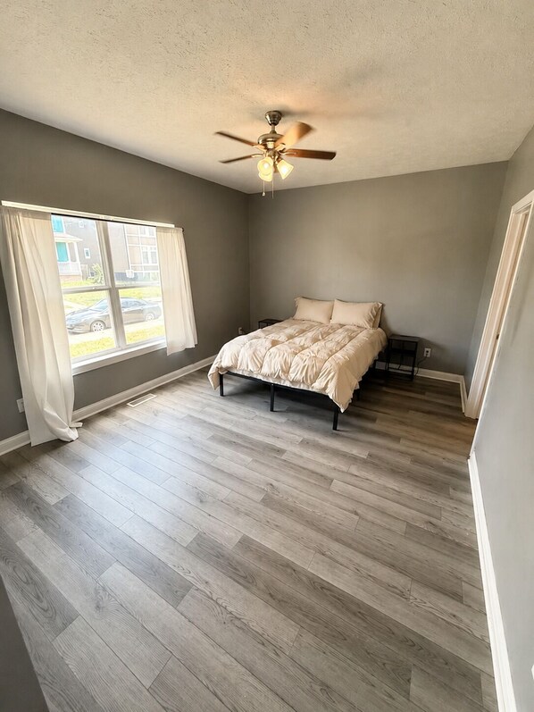 Une chambre à coucher avec un lit, un ventilateur de plafond et une fenêtre avec des rideaux.