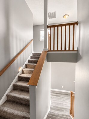 Eine Treppe mit hölzernen Geländern, Teppichstufen und einer Leuchte auf der Zwischenebene.