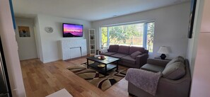 Ein Wohnzimmer mit Fernseher, einer Couch, einem Couchtisch und einem Kamin.