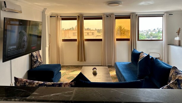 A living room with a sofa, a television, and a view of buildings through the windows.