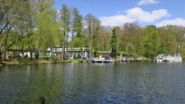 A lakeside property with docked boats, a house with a green roof, and trees surrounding the area. - Ferienwohnung mit Blick auf den Glindower See (Werder (Havel))