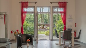 A room with a sofa, a table with a vase, a chair, and a view through glass doors to an outdoor area with a table and chairs. - Ferienwohnung mit Blick auf den Glindower See (Werder (Havel))