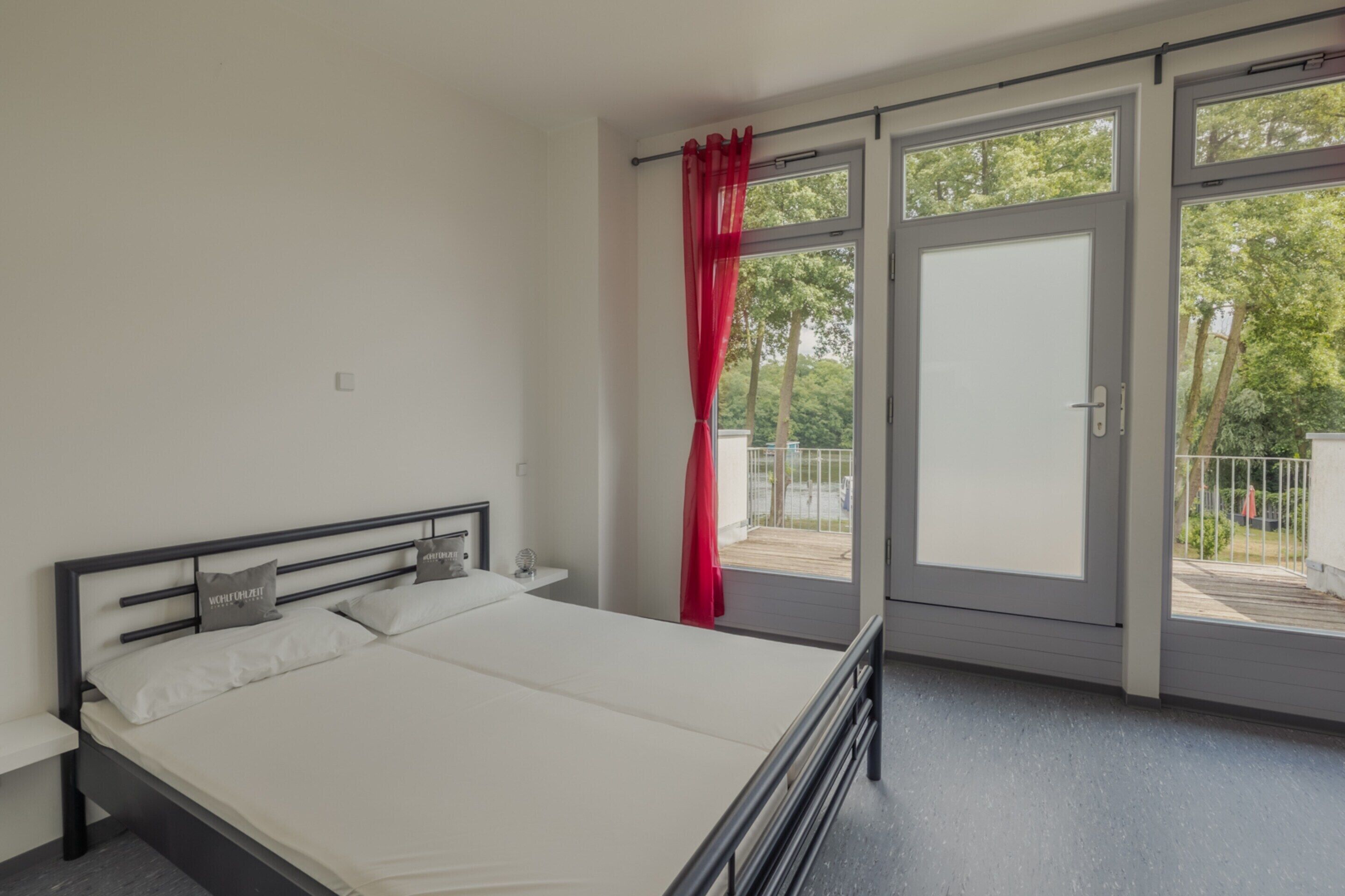 A bedroom with a bed, a nightstand, a window with a curtain, and a door leading to an outdoor area.