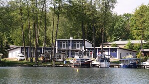 A lakeside property with docked boats, a white van, and a building with a balcony. - Ferienwohnung mit Blick auf den Glindower See (Werder (Havel))