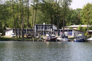 A lakeside property with docked boats, a white van, and a building with a balcony. - Ferienwohnung mit Blick auf den Glindower See (Werder (Havel))