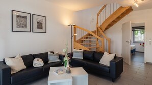 A modern living room with a black sofa, a white coffee table, and a wooden staircase. - Ferienwohnung mit Blick auf den Glindower See (Werder (Havel))