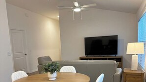 Een moderne woonkamer met een eettafel, stoelen, een bank, een televisie en een plafondventilator.