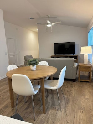 Ein modernes Wohnzimmer mit Esstisch, Stühlen, einer Couch, einem Fernseher und einem Deckenventilator.