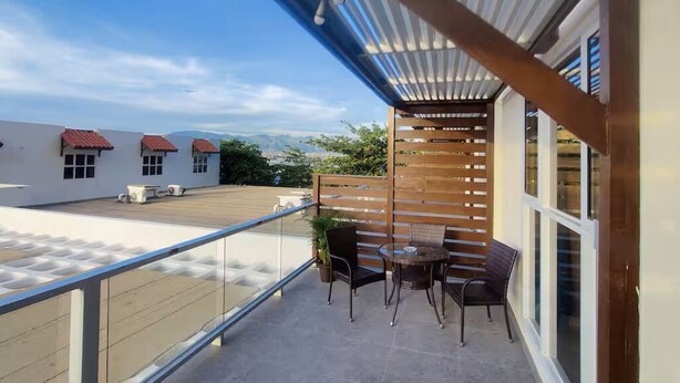 Ein Balkon mit Tisch und Stühlen, eine Holzlamellenwand und Blick auf Gebäude und Grünflächen.