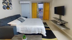 Ein Schlafzimmer mit Bett, einer Couch, einem Fernseher und Blick durch eine Tür.