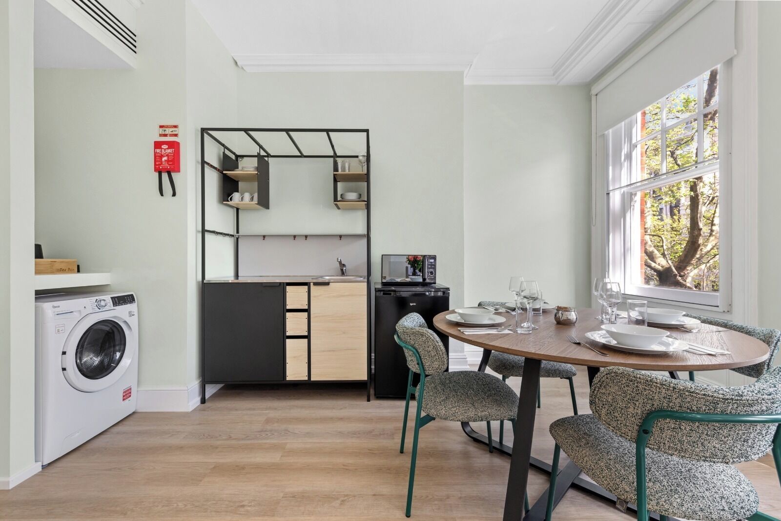 Een kleine keuken met een wasmachine, een eettafel met stoelen en uitzicht door een raam.