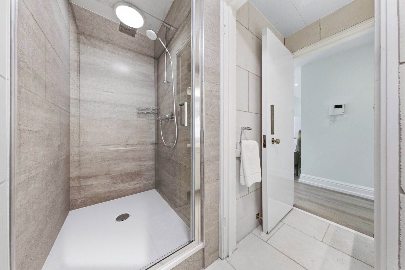 A modern bathroom with a glass-enclosed shower, a white bathtub, and a door leading to another room.