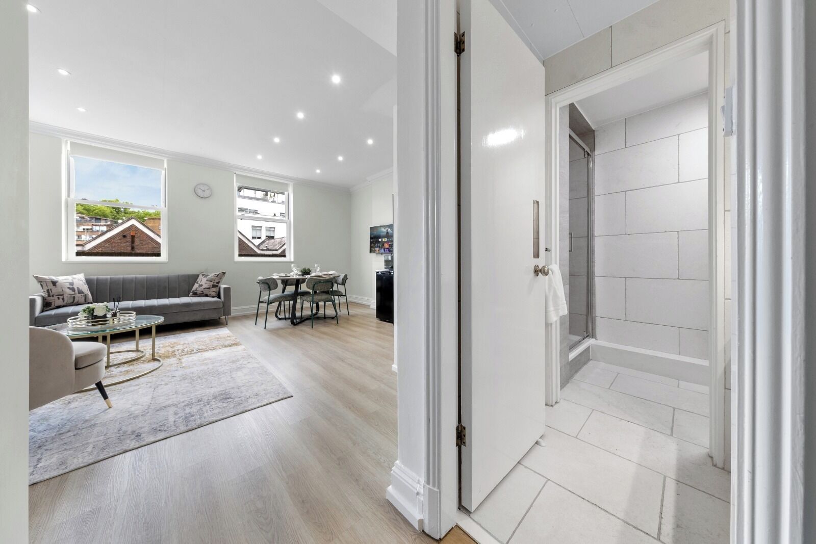 Un salon moderne avec un canapé, une table basse et un coin repas, une salle de bain carrelée de blanc et une vue sur l’extérieur.