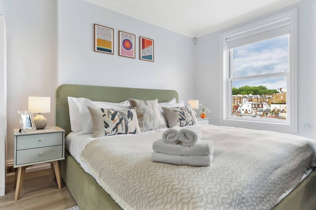 A neatly arranged bedroom with a large bed, bedside tables, and a window with a city view.