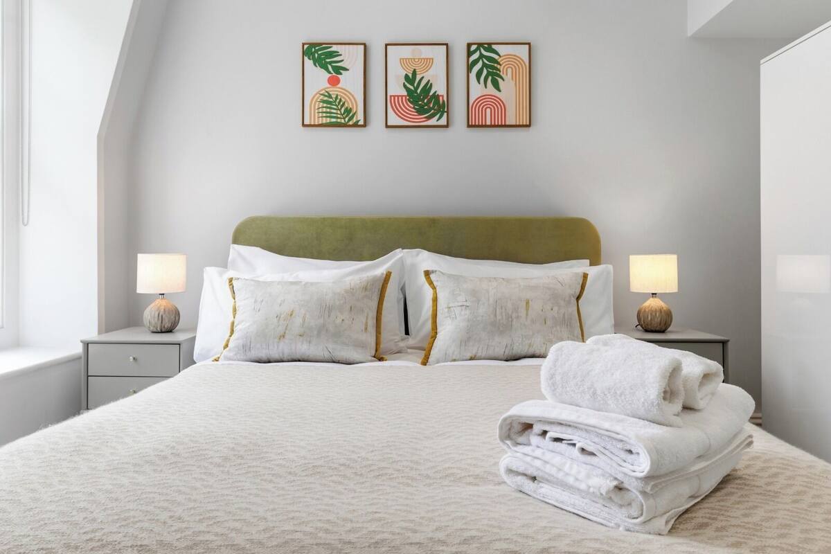 A neatly made bed with white linens, two bedside lamps, and three framed artworks on the wall.