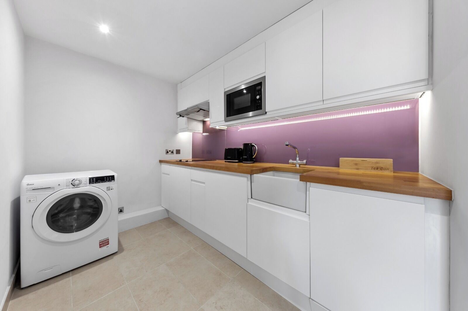 Een kleine keuken met een wasmachine, een magnetron en een spoelbak met een houten aanrecht.