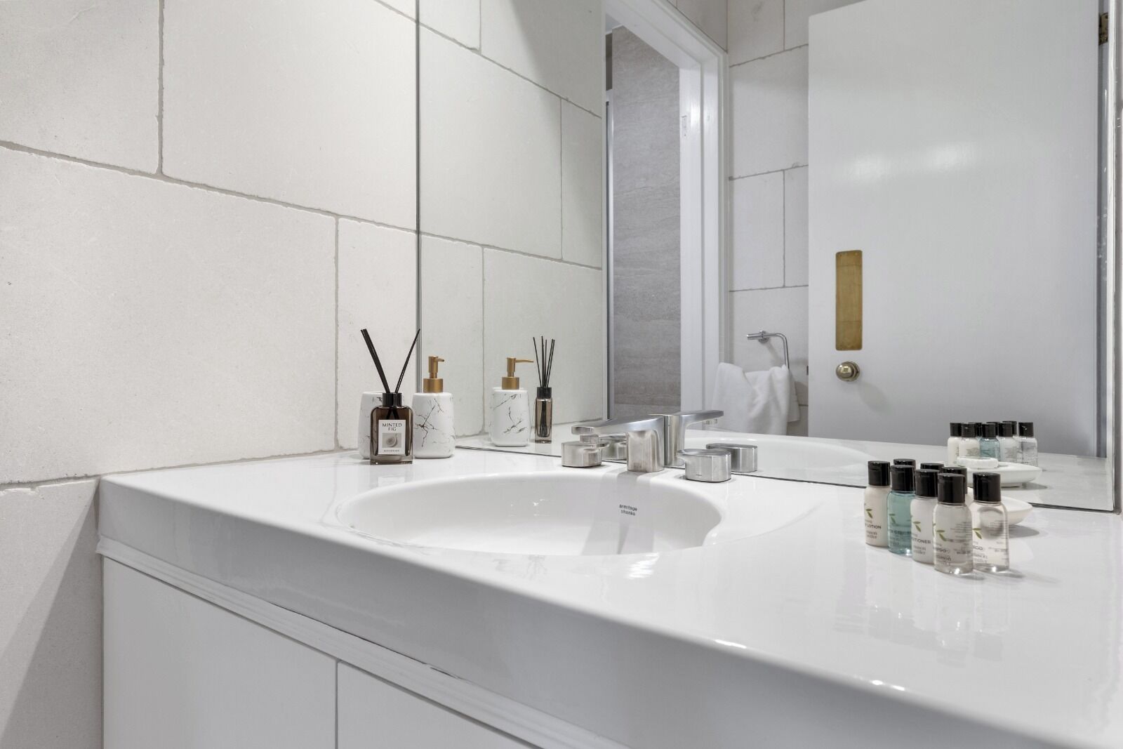 Un baño moderno con un lavamanos blanco, un espejo y diversos artículos de aseo.
