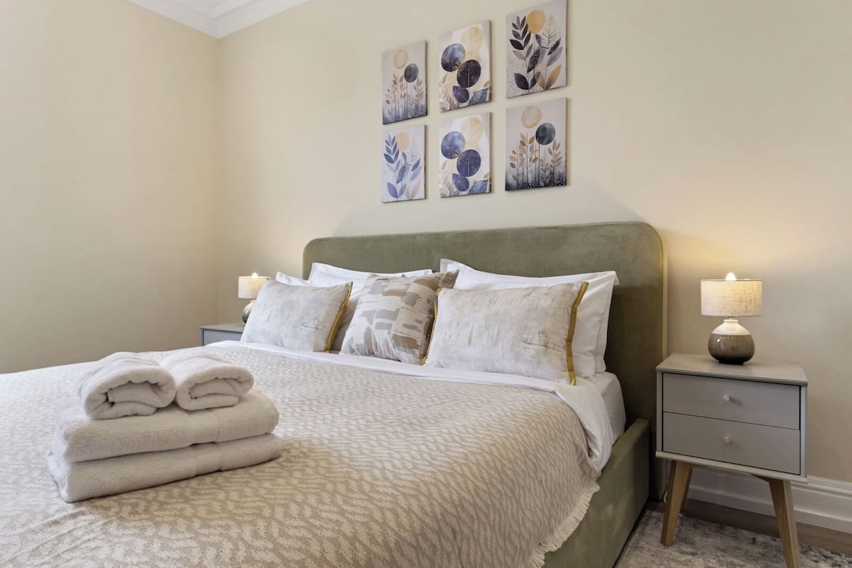 A neatly made bed with a white comforter and pillows, a bedside lamp, and artwork on the wall.