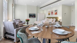 A modern hotel room with a round dining table set for four, a sofa, a TV, and a bed with a headboard. - BAZ Tower - London (London)