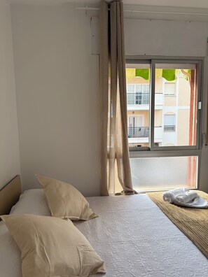 Ein Hotelzimmer mit Bett, zwei Kissen, einem Fenster mit Vorhängen und Blick auf Gebäude.