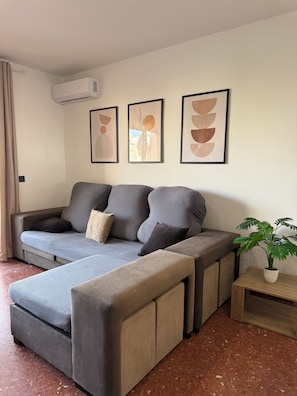 Ein modernes Wohnzimmer mit einem grauen Sofa, einem kleinen Holztisch und einer Topfpflanze.