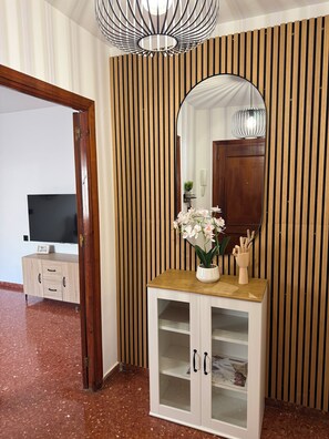 Ein Zimmer mit einer Wand aus Holzlatten, einem weißen Schrank mit Glastüren, einem Spiegel, einem Topf mit einer Orchidee und einem Fernseher auf einem Holzschrank.