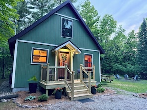 A green wooden house with a porch, a staircase, and a small garden area.