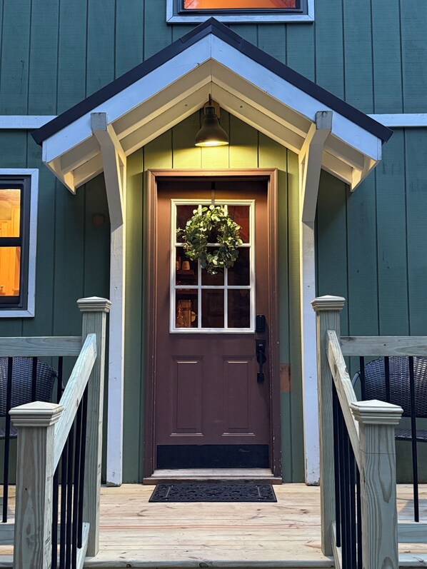 A green building with a brown front door, white trim, and a black mailbox.