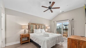 Quarto com cama, mesas de cabeceira, ventilador de teto e vista para o exterior.