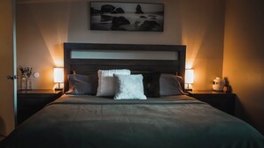 Un lit bien fait, avec des oreillers, une tête de lit, des lampes de chevet et un tableau encadré accroché au mur.