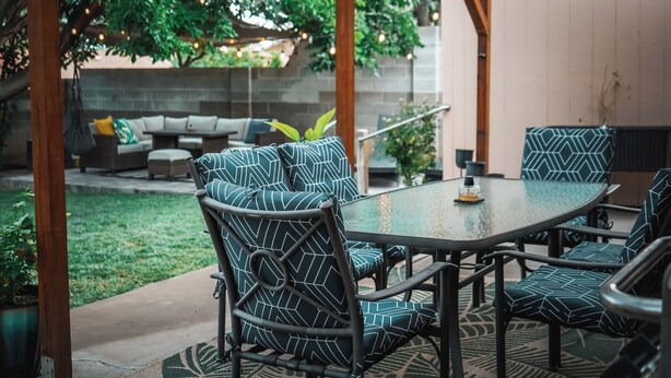 Une terrasse extérieure avec une table et des chaises, un espace salon couvert et un jardin.