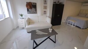 En moderne stue med en hvid sofa, et gråt sofabord, et sort skab og en stribet seng.