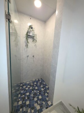 Une douche avec une porte en verre, un sol carrelé et un luminaire au plafond.