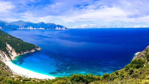 Paesaggio costiero con vista aperta sul mare, una spiaggia e una catena montuosa.
