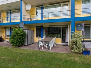 En toetages bygning med balkon, parabolantenner og et spiseområde med udendørs siddepladser.