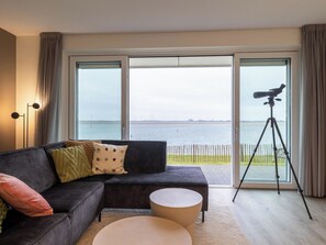 Un salon moderne avec une grande fenêtre, un canapé, une table basse et un télescope monté sur un trépied.