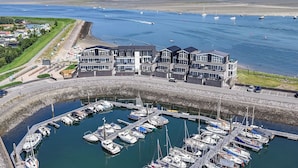 A marina with boats docked, a building with multiple balconies, and a view of the sea and wind turbines in the distance. - Lumen Mare by Interhome (Sint-Annaland)