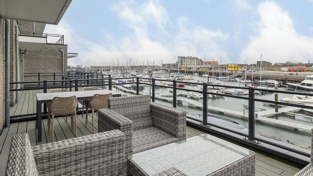 A deck with wicker furniture overlooking a marina with boats. - Lumen Mare by Interhome (Sint-Annaland)