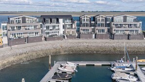 A waterfront property with multiple modern buildings, a dock with boats, and a view of wind turbines in the distance. - Lumen Mare by Interhome (Sint-Annaland)