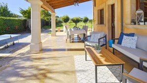 Een terras buiten met een houten pergola, een tafel, stoelen en een bank.