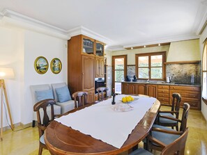 A dining area with a long wooden table, chairs, a sofa, and a kitchen with wooden cabinets and a window. - Tranquil Binissalem Country Home With Pool (Binissalem)