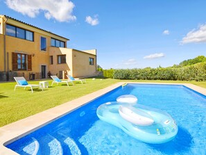 A swimming pool with lounge chairs and inflatable rings, a house with a tiled roof, and a well-maintained lawn. - Tranquil Binissalem Country Home With Pool (Binissalem)