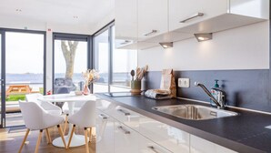 Et moderne køkken med et stort vindue, et spiseområde med hvide stole og havudsigt.