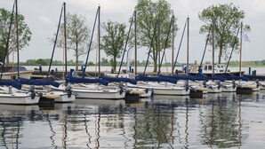 En lystbådehavn med flere både i havnen, træer i baggrunden og stille vand.
