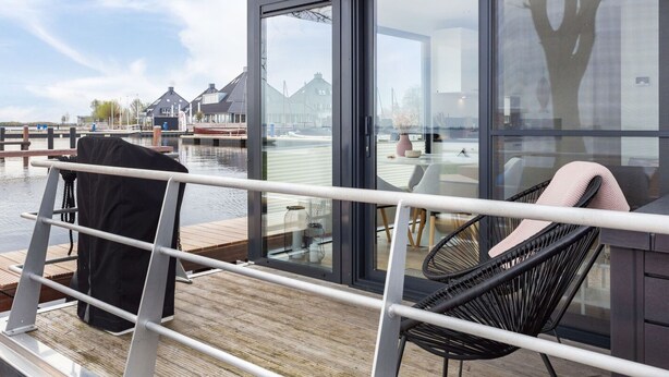 En træterrasse med en stol, et bord, et gelænder og udsigt over en kanal med bygninger.
