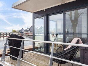 Une terrasse avec une chaise et une table, une rambarde et une vue sur un canal bordé d’immeubles.