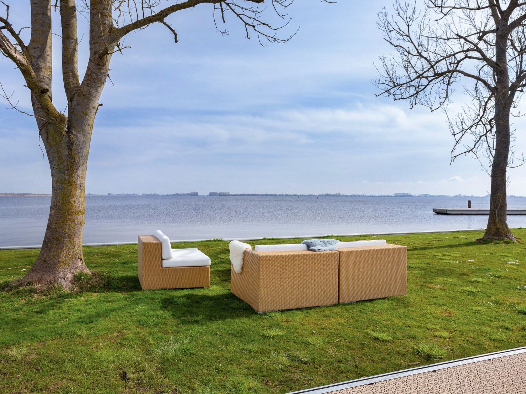 A grassy area with two wicker sofas and a small table, overlooking a body of water.